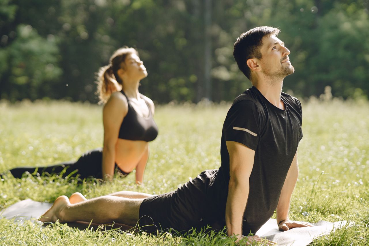 services-01 Man and woman stretching in an outdoor yoga session in a sunny field.