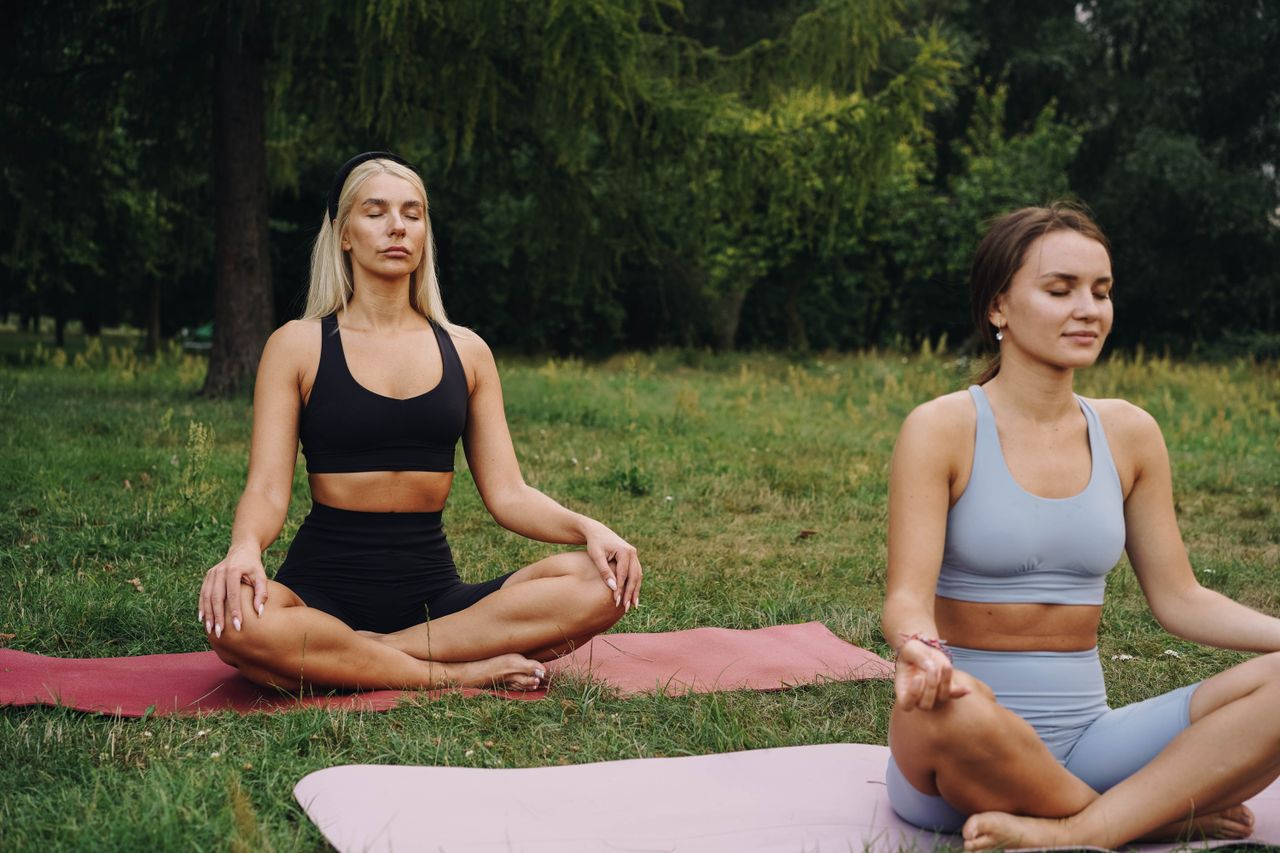 services-bg Two women meditating on yoga mats in a tranquil park, promoting mindfulness and relaxation.